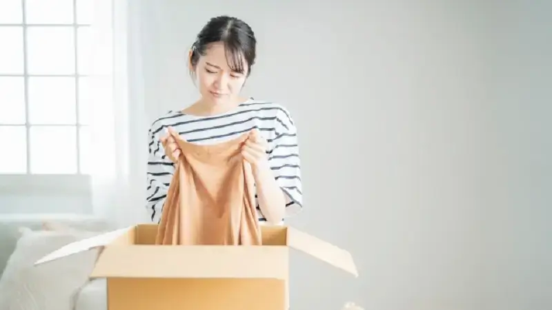 段ボールから出した服を見て不満そうな顔をする女性